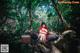 A woman in a red riding hoodie sitting on a rock in the woods.