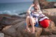 A woman in a sailor outfit sitting on a rock by the ocean.