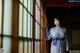 A woman in a kimono standing in front of a window.