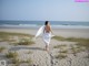 A woman walking on a sandy beach with a white scarf around her neck.